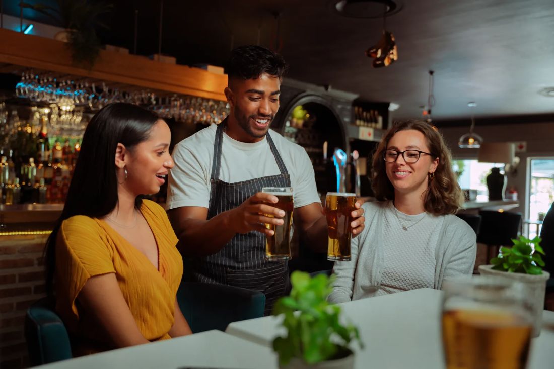 Garçom servindo chope para clientes na mesa do bar