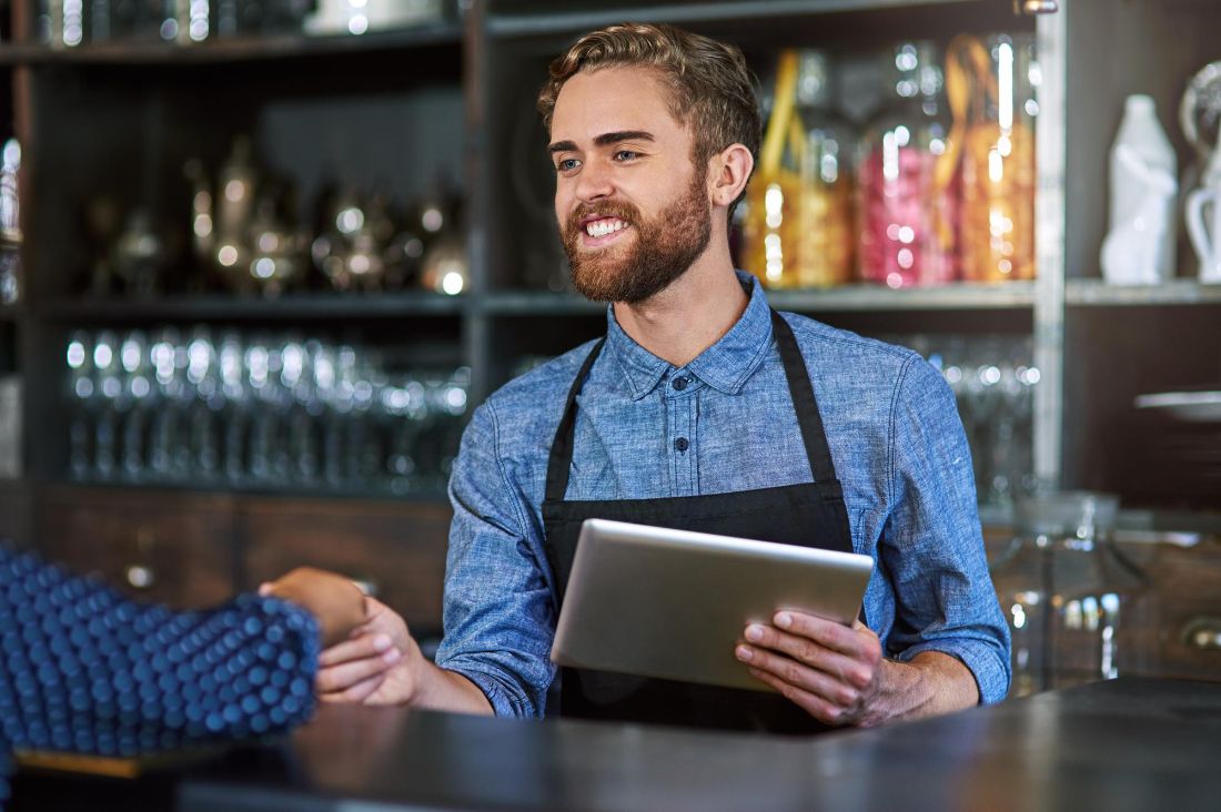 Barman atendendo o cliente no balcão com o tablet na mão