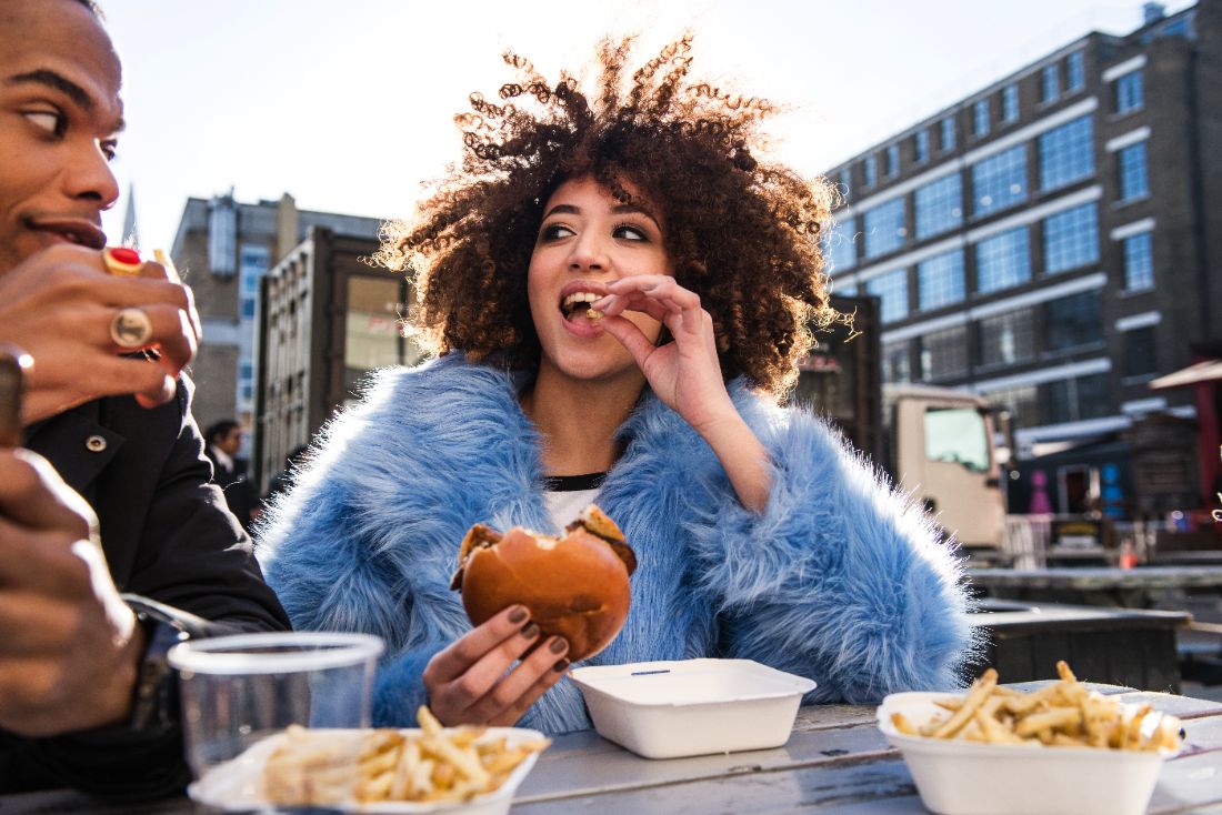 Clientes comendo hambúrguer e fritas na mesa externa