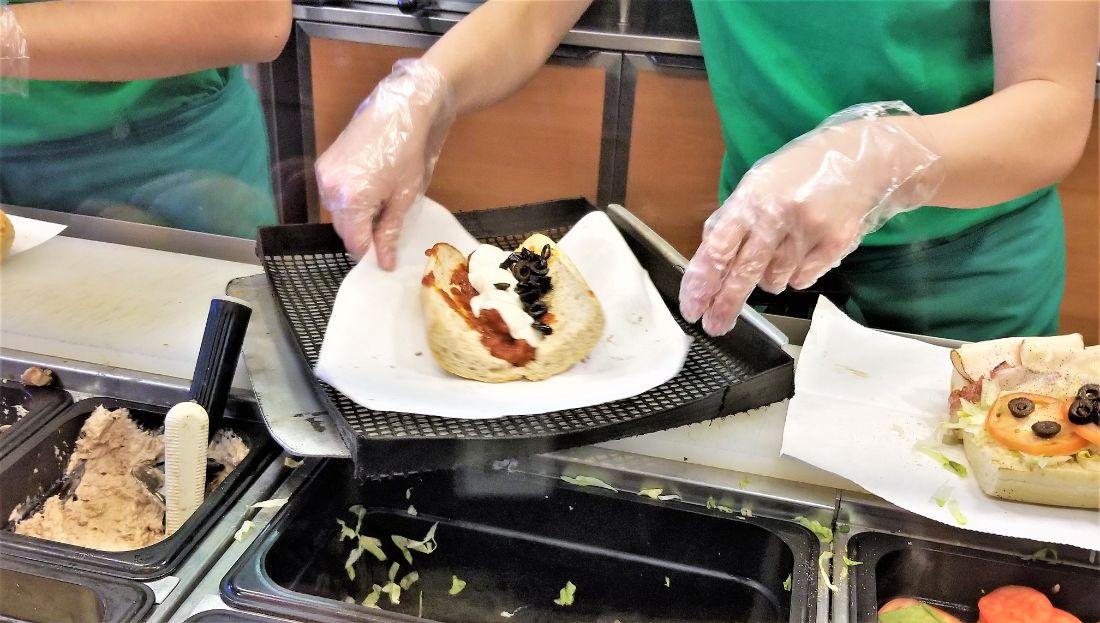 Atendente montando o sanduíche no balcão de produção