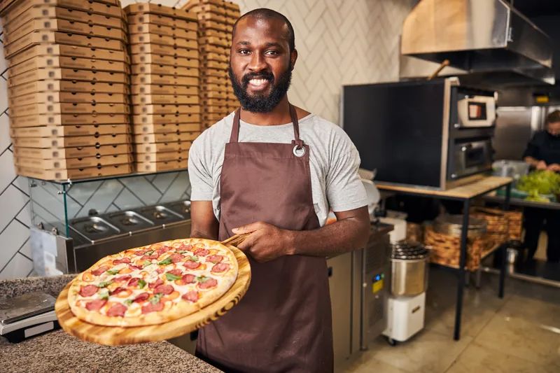 Atendente apresentando a pizza pronta no balcão